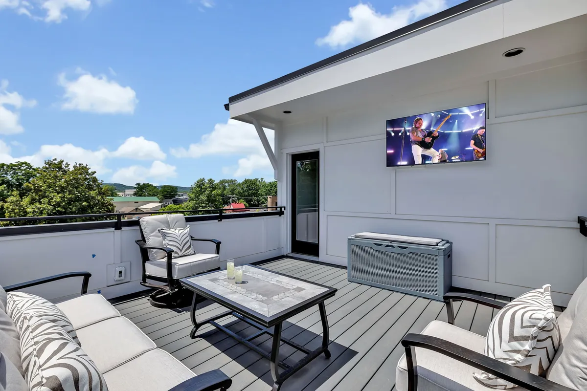This image displays a stylish rooftop seating area with comfortable chairs, an outdoor television, a decorative table, and a breathtaking scenic view. The setting is casual yet upscale, perfect for both entertainment and relaxation.