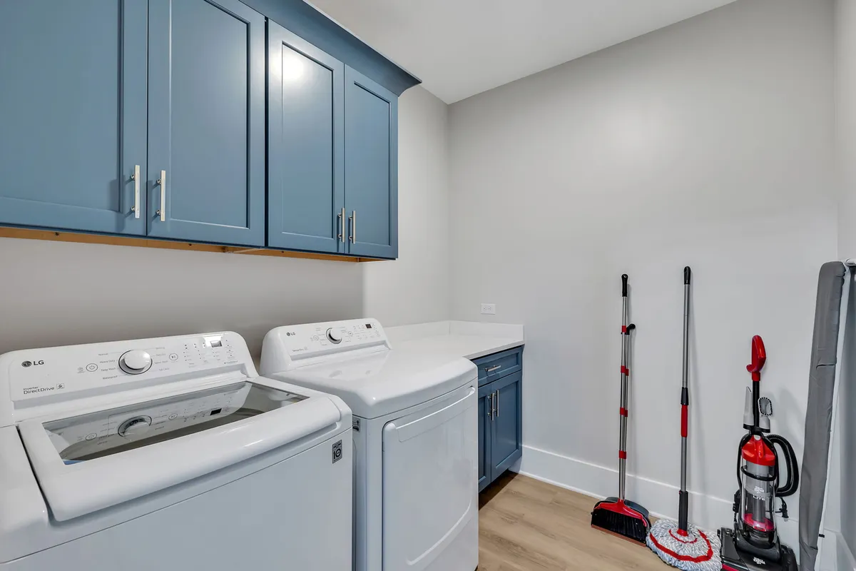 A well-organized laundry area featuring a washing machine and dryer, complemented by blue cabinets and cleaning supplies. The space is practical and tidy, emphasizing utility and convenience for guests.