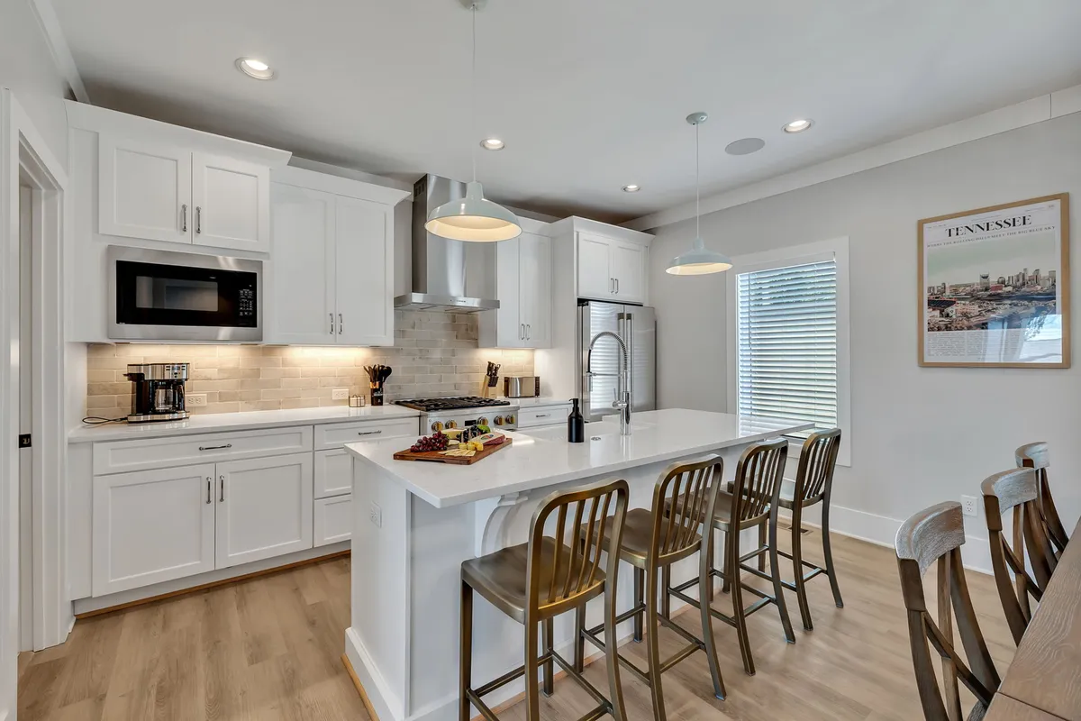 A modern kitchen with a spacious island, sleek bar stools, Monogram stainless steel appliances, and warm wooden accents. The inviting setup suggests a space designed for cooking, entertaining, and casual dining.