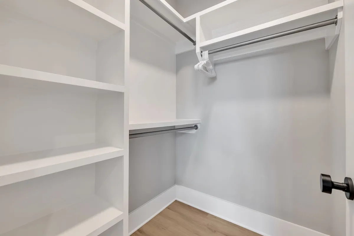 A minimalist closet with shelves and a hanging rod, providing ample space for organizing clothes and storing personal items. The clean, uncluttered design highlights ease of use.