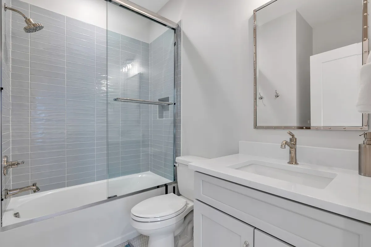A modern bathroom with a large glass shower enclosure, a sleek vanity and sink, and a generously sized mirror. The space feels fresh, bright, and designed for rejuvenation, ideal for both quick morning routines and relaxing evening refreshes.